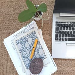 La imagen muestra una composición de diversos objetos relacionados con la traducción para expresar la idea del servicio «Otras traducciones». Aparecen una pluma estilográfica sobre dos cuadernos y unos documentos jurídicos, una planta pequeña y parte del teclado y la pantalla de un ordenador portátil.