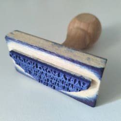Tampón de madera con letras manchadas con tinta azul en el que se ven escritos los datos de Marta Mozo como traductora jurada y que utiliza para sellar las certificaciones de las traducciones juradas.